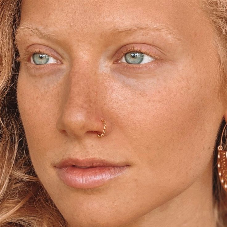 a close up of a woman with freckles on her nose and piercings