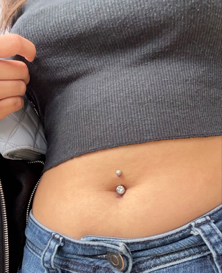 a woman's stomach with a piercing on the side and a zippered jacket behind her