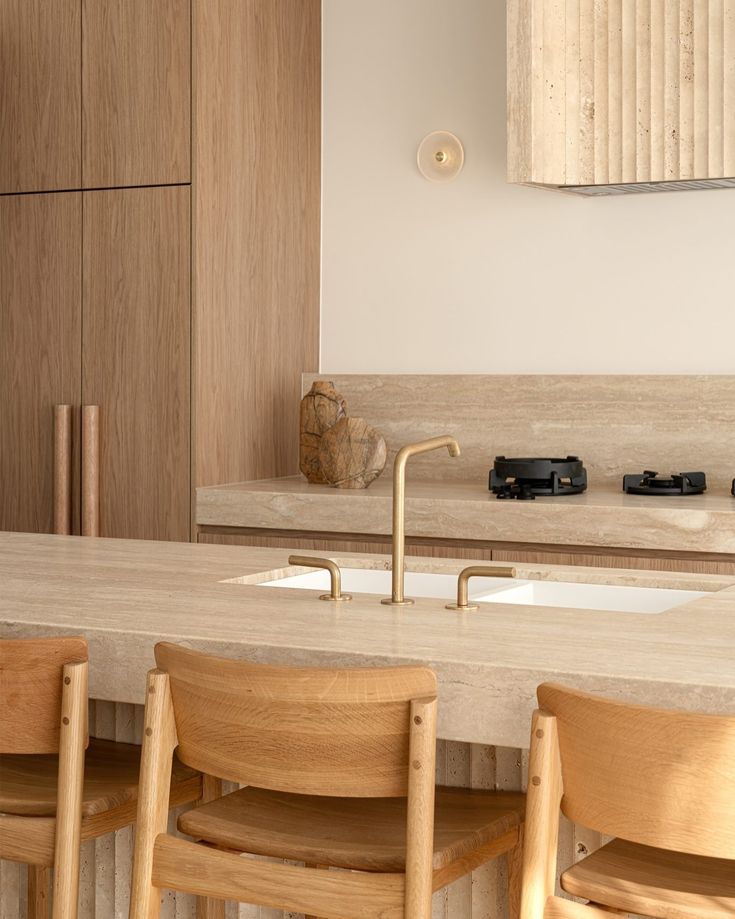 a kitchen counter with four wooden chairs and a sink in the middle, next to cabinets