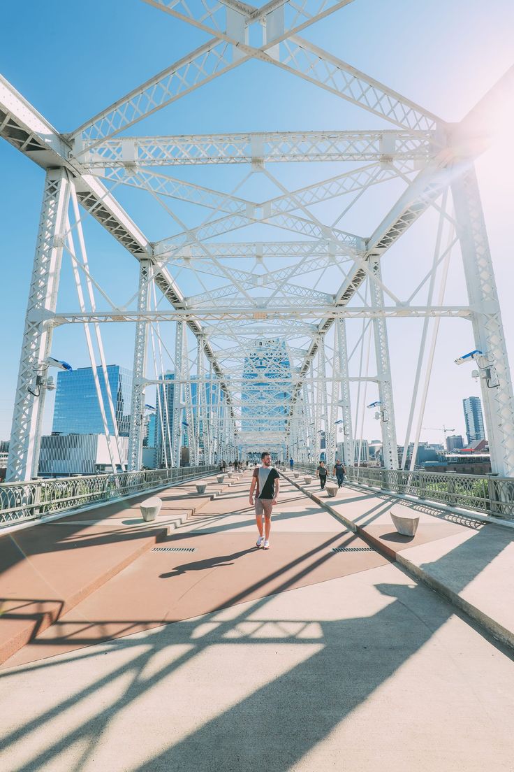 two people walking across a bridge with the sun shining on them and buildings in the background