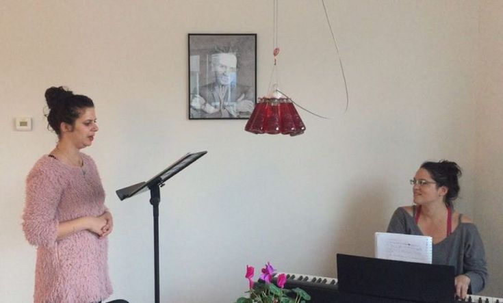 two women are standing in front of a microphone and playing music on the keyboard while another woman is sitting at a piano behind them