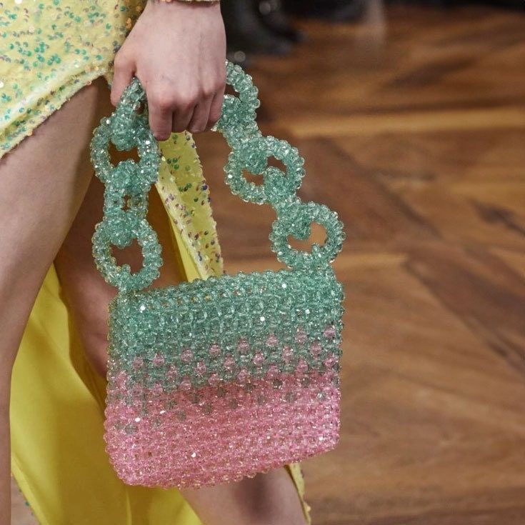 a woman's hand holding a pink and green beaded purse on top of a wooden floor