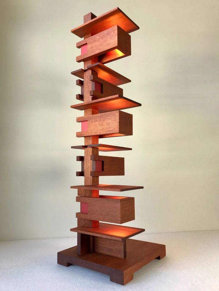 a tall wooden sculpture sitting on top of a white table next to a light bulb