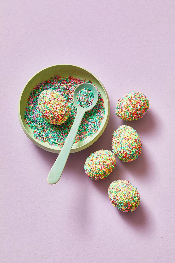 sprinkle covered donuts in a bowl with a spoon next to them on a pink surface