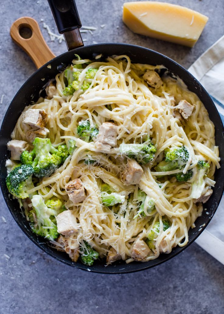 a skillet filled with pasta, broccoli and chicken on top of a table