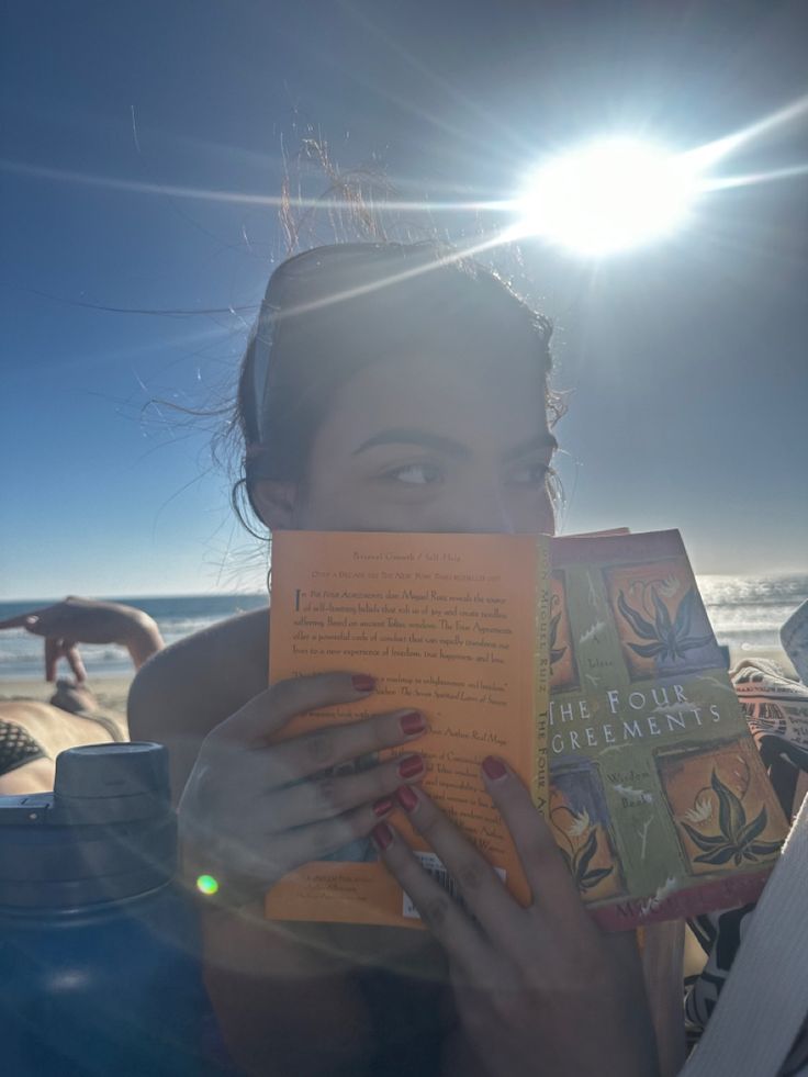 a woman is reading a book on the beach while sun shines in the background