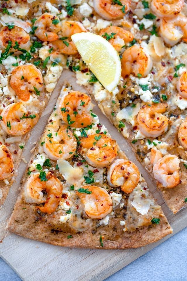 a pizza topped with shrimp and cheese on top of a wooden cutting board