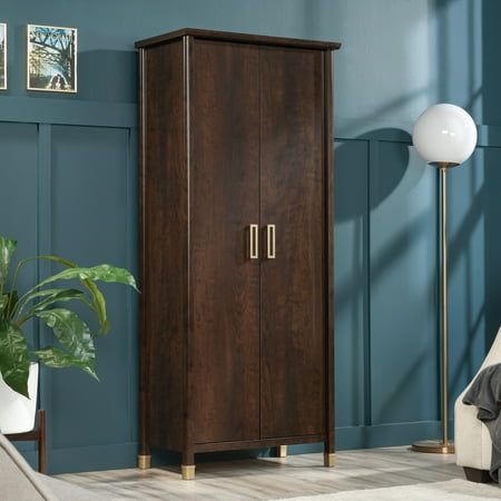 a tall wooden cabinet sitting in a living room next to a white chair and potted plant