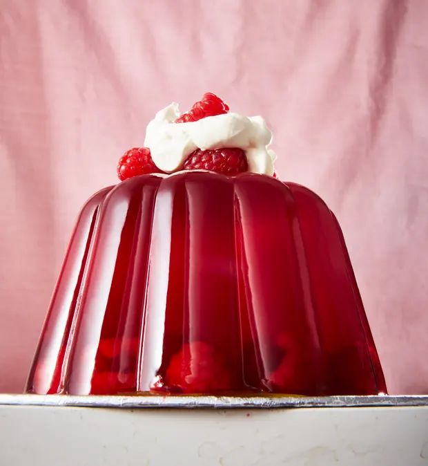 raspberry jelly pudding with whipped cream and fresh berries on top, ready to be eaten