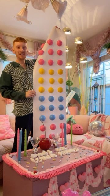 a man standing next to a giant cake in a living room filled with pink and blue decorations