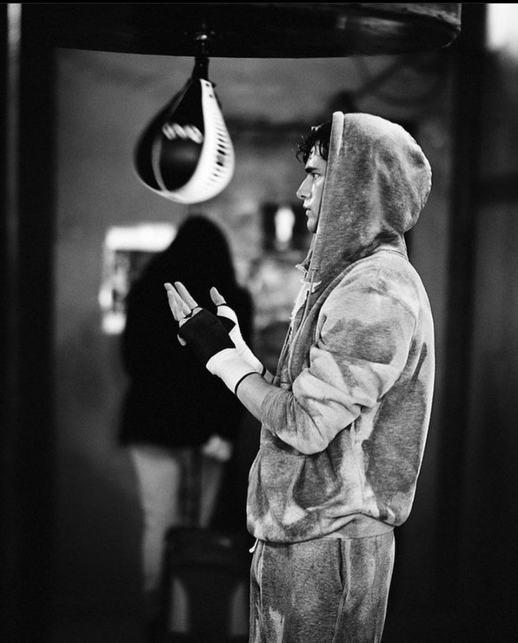 a man in a hoodie is holding his hand out to someone wearing a boxing glove