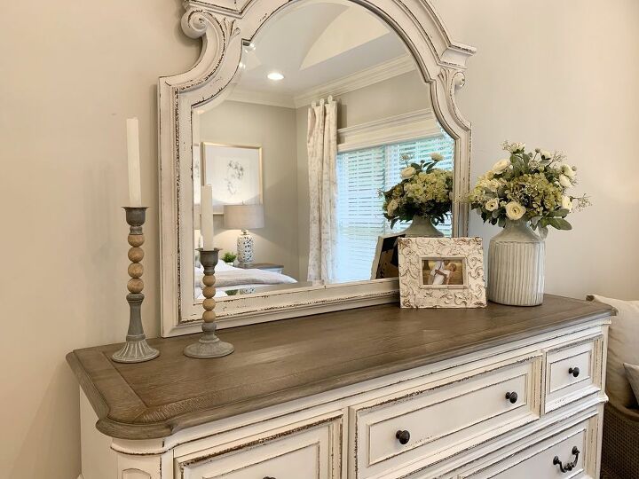 a white dresser topped with a mirror and vase filled with flowers