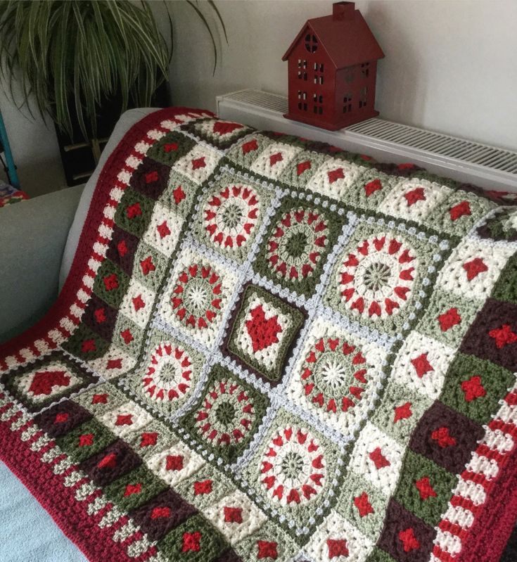 a crocheted granny blanket on a couch next to a potted plant and bird house