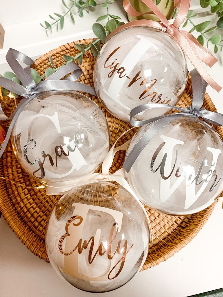 four clear glass ornaments with the word merry written on each ornament and ribbon tied around them