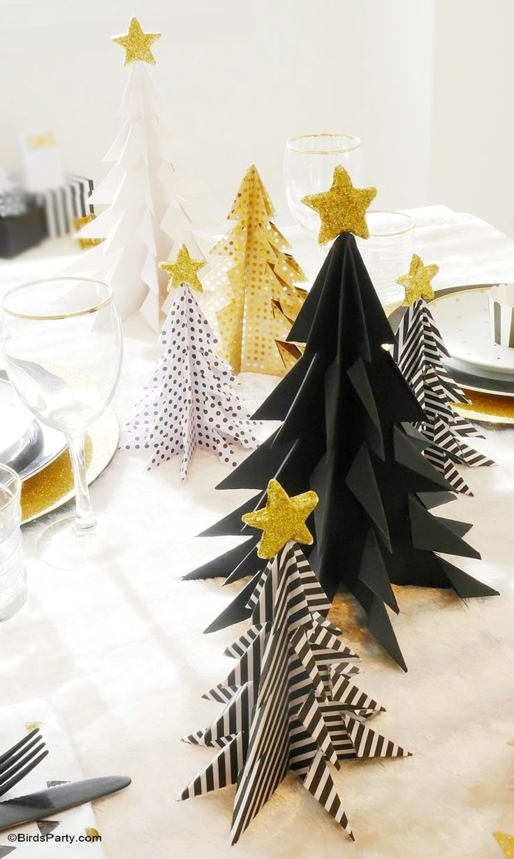 black and white paper christmas trees on a table with gold stars, napkins and plates