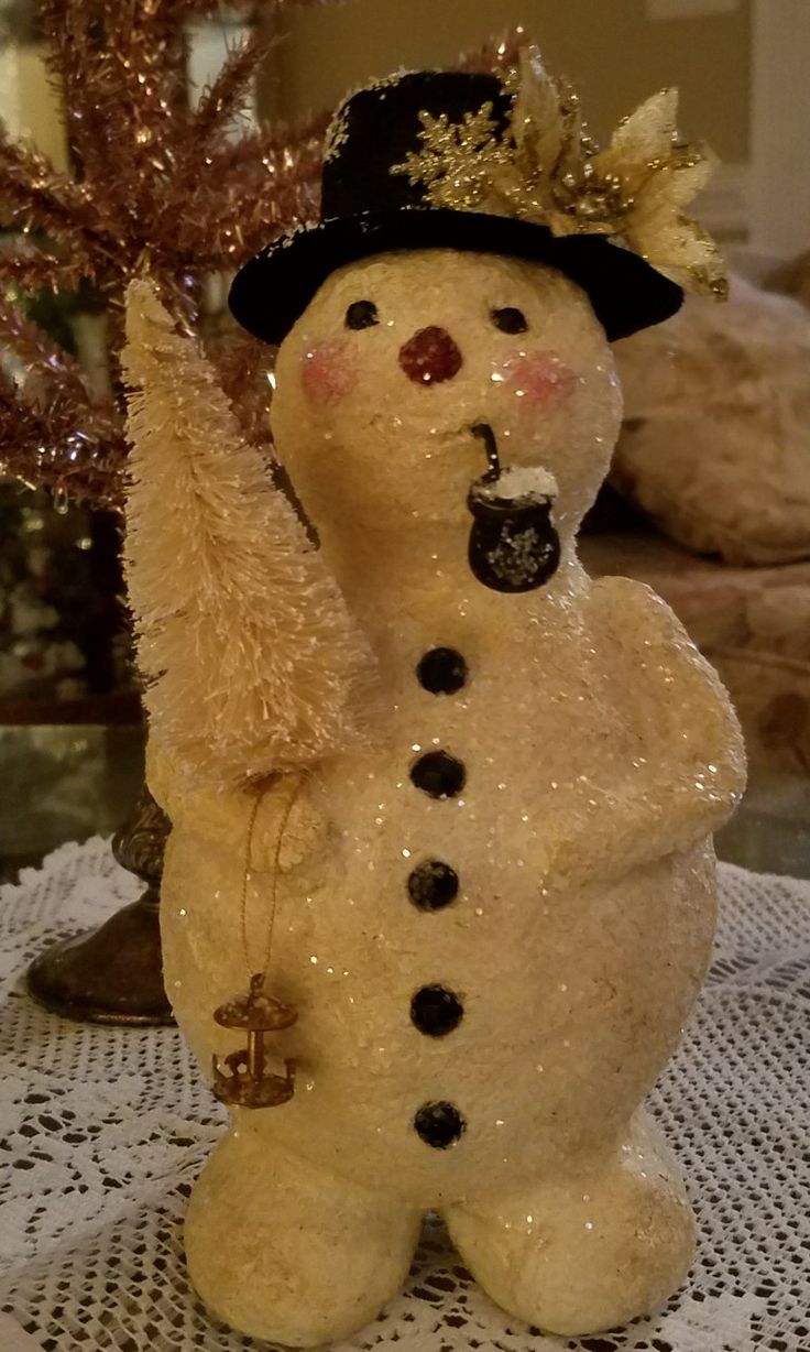 a snowman figurine on a table with a christmas tree in the background