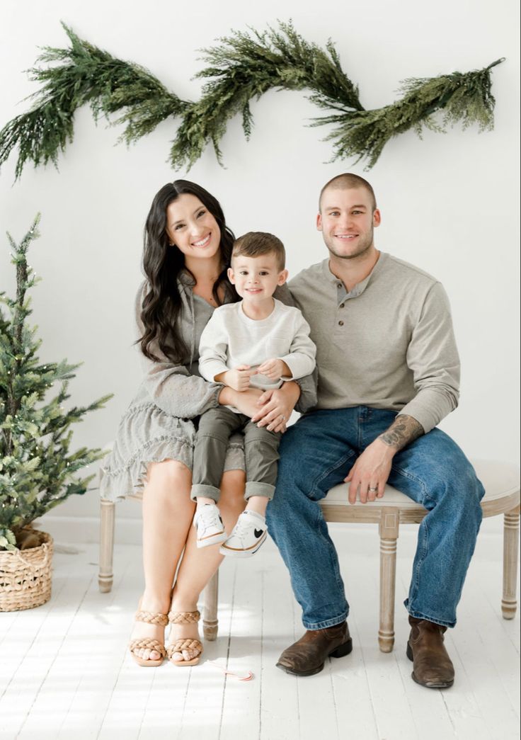 a man and woman sitting on a bench with a baby in front of christmas trees