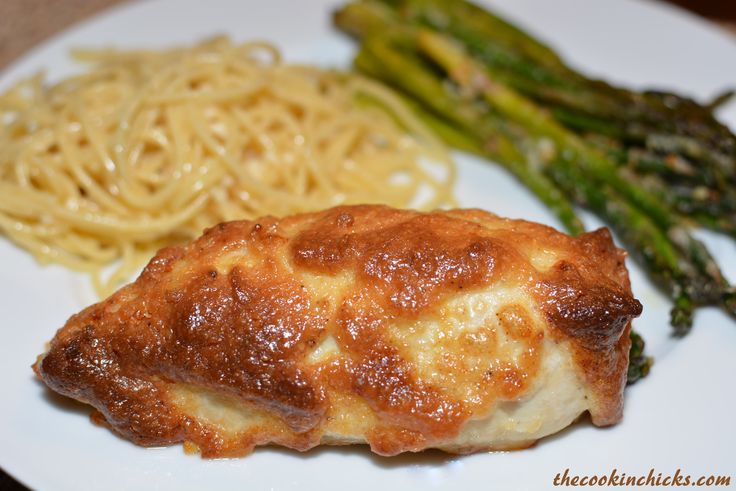 a white plate topped with pasta and meat covered in sauce next to asparagus