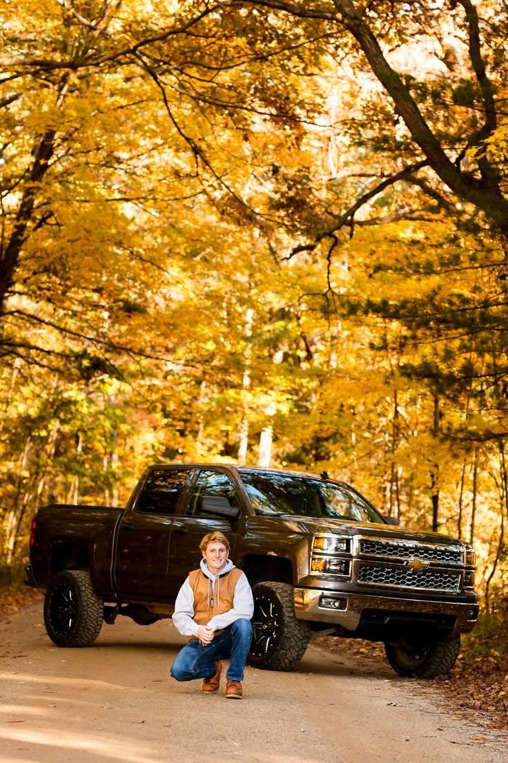 a man kneeling down next to a truck on a dirt road in the fall leaves