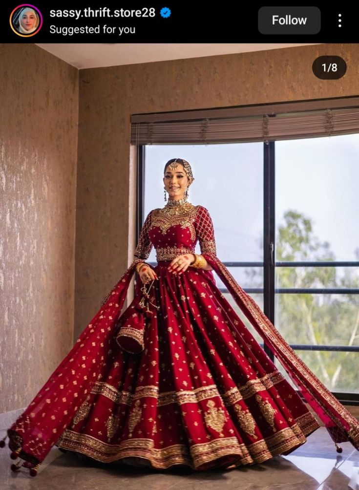 a woman in a red and gold bridal gown standing by a window with her hands on her hips