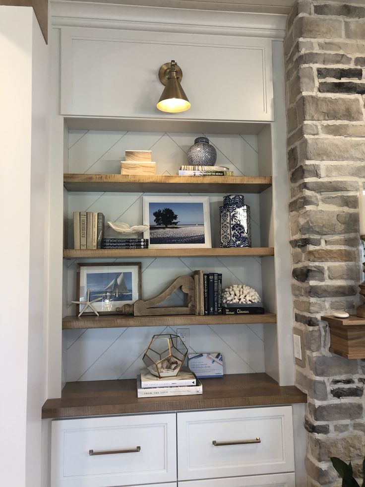 a book shelf with books and pictures on it next to a brick wall in a living room