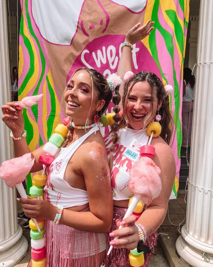 two women in pink and white outfits standing next to each other with candy on their heads