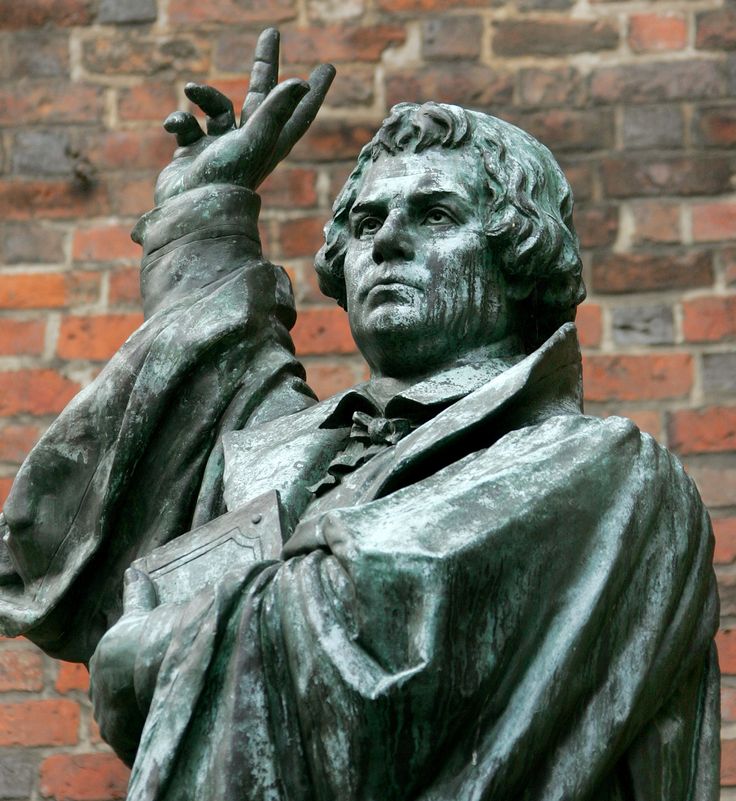 a statue of a man holding his hand up to the sky in front of a brick wall