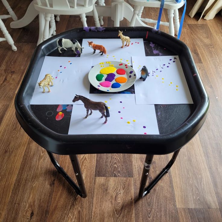 a child's art table with paint, paper and horses on it in front of chairs