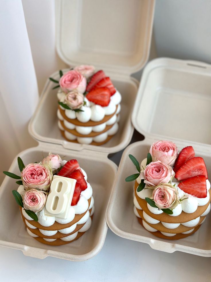 four cupcakes with strawberries and roses on them are arranged in small trays