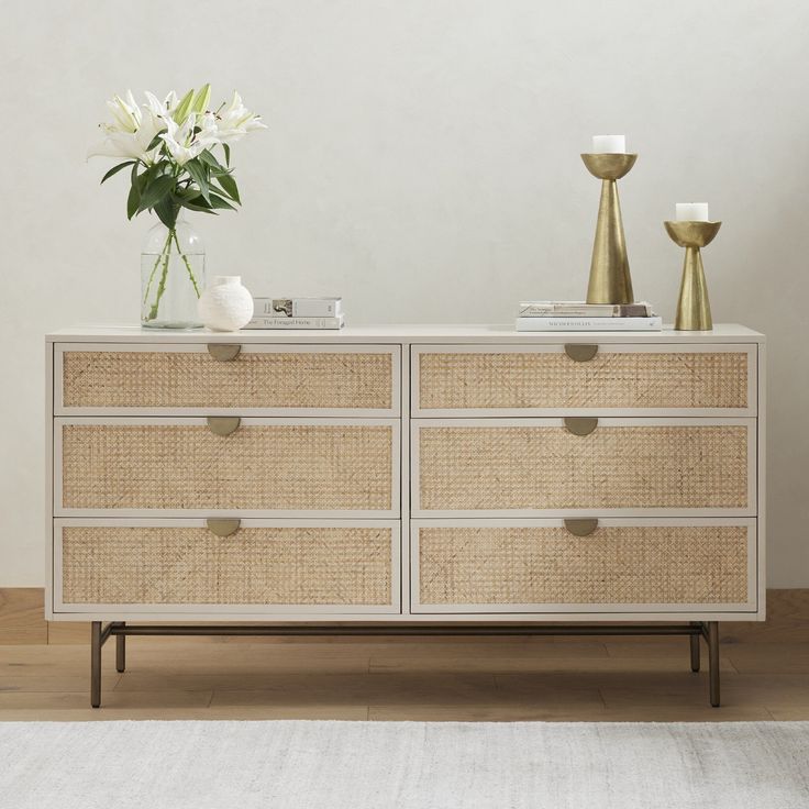 a white and beige dresser with some flowers on top of it in front of a wall