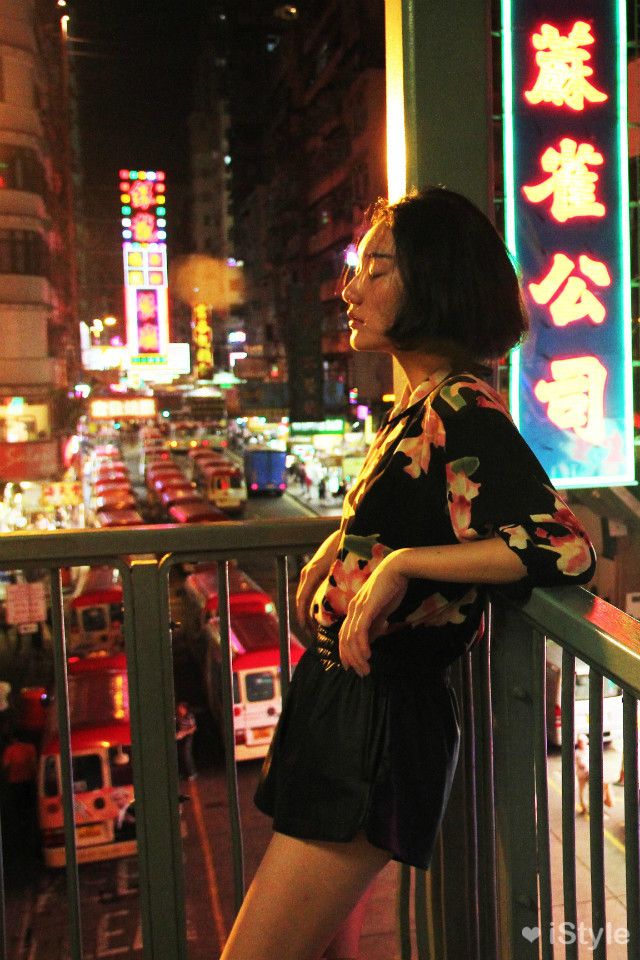 a woman standing on top of a balcony next to a traffic filled city at night