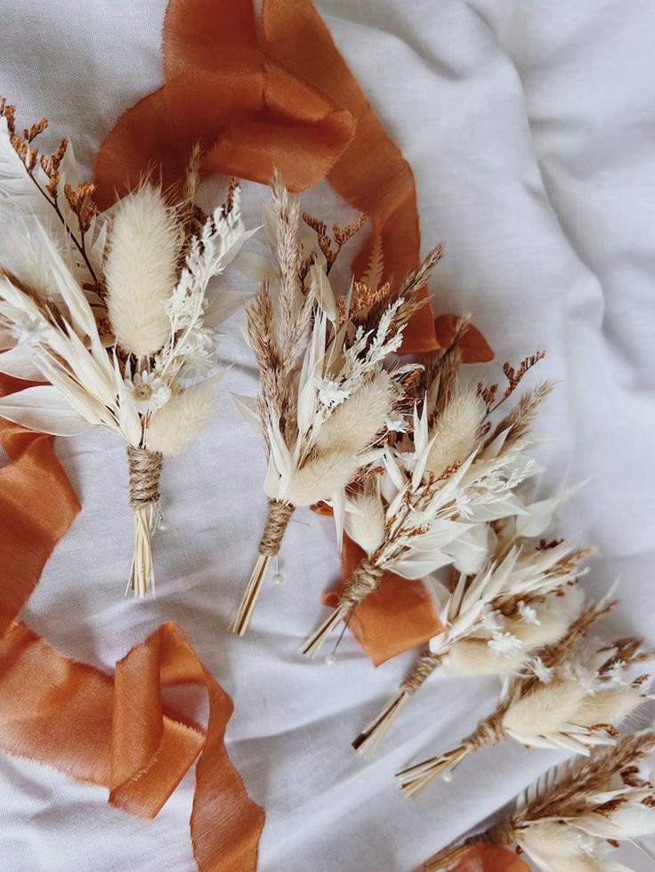 three dried flowers on a white sheet with orange ribbon around the stems and petals in between them