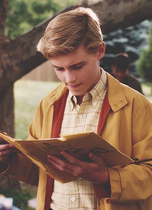 a young man reading a book under a tree