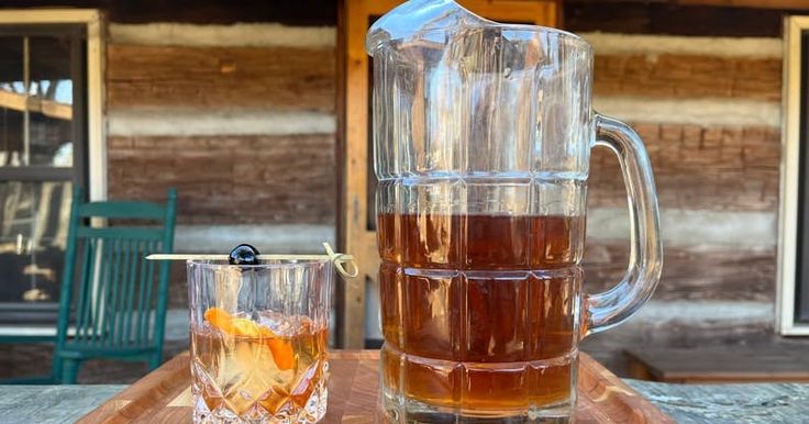 a pitcher and glass filled with liquid sitting on top of a wooden table next to each other