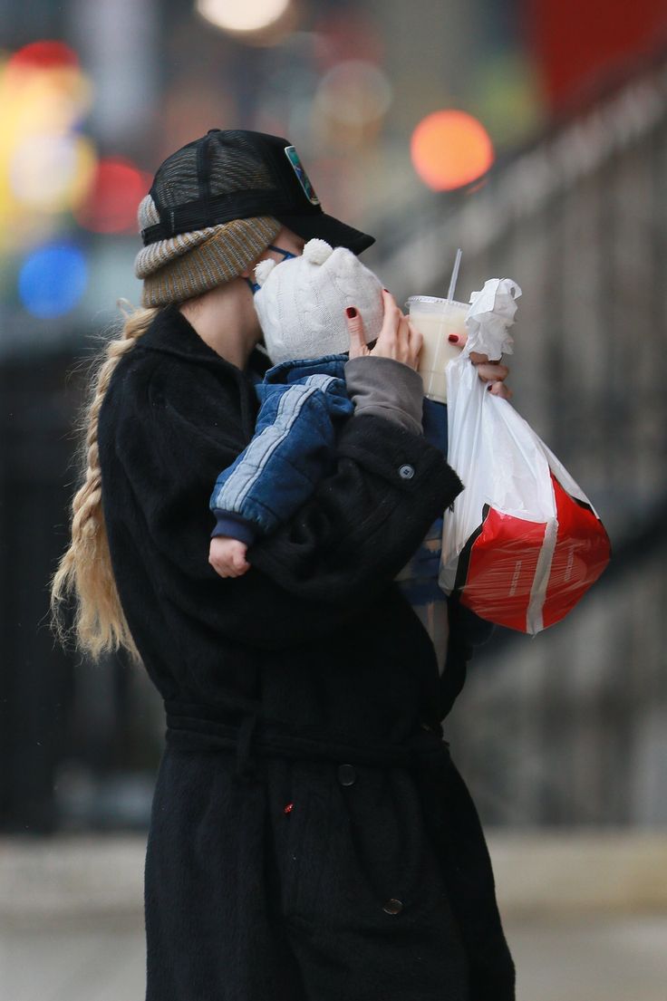 a woman holding a baby in her arms while walking down the street with other people