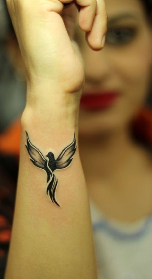 a woman's arm with a bird tattoo on the left side of her wrist