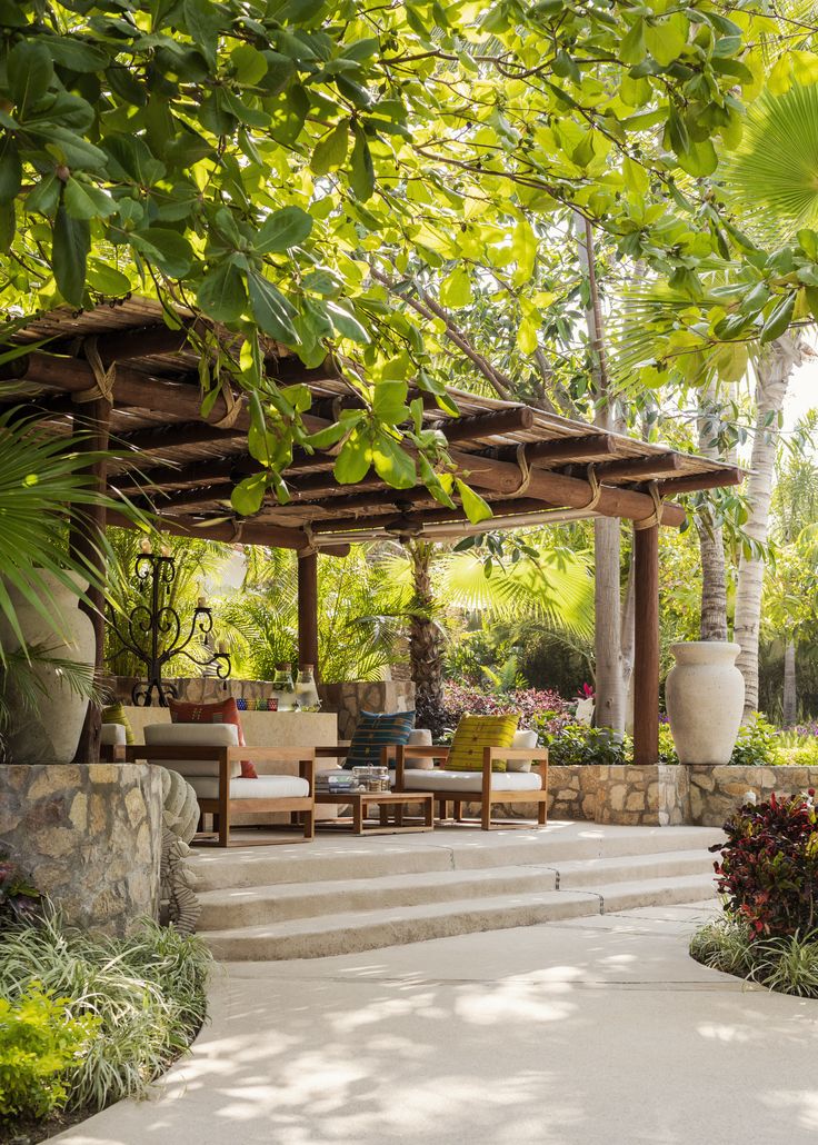 an outdoor living area with stone steps and seating under a pergolated roof surrounded by greenery