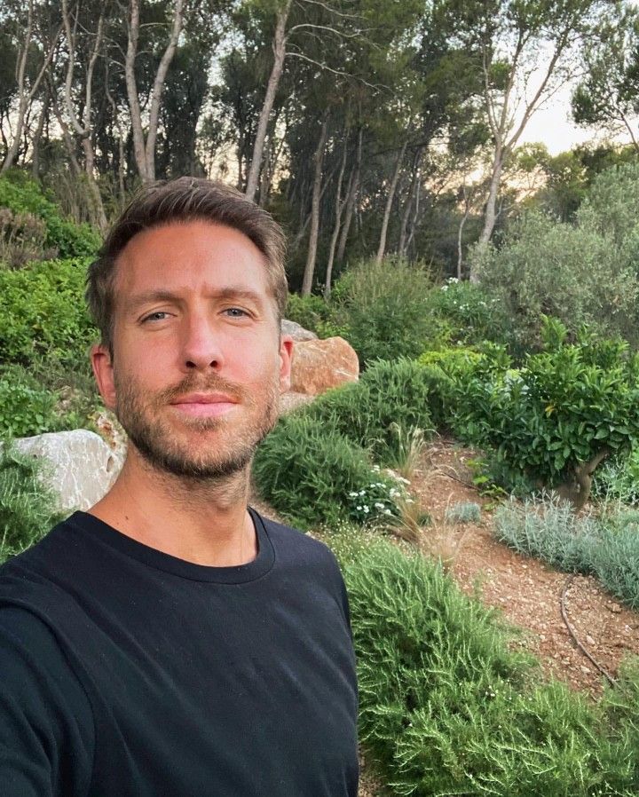 a man standing in front of a lush green hillside with trees and bushes on the side