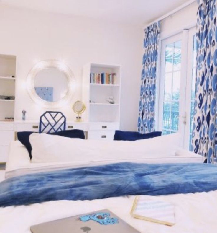 a laptop computer sitting on top of a bed next to a blue and white curtain