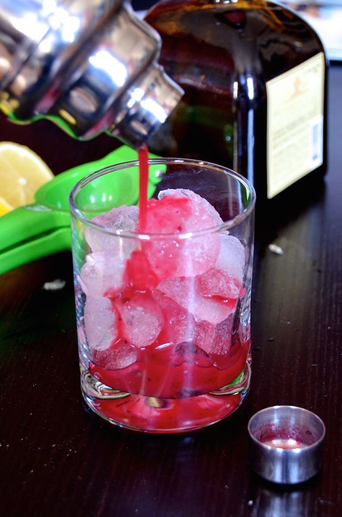 a glass filled with ice sitting on top of a wooden table next to a bottle