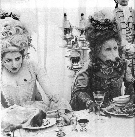 three women dressed in fancy costumes sitting at a table with food and drinks on it