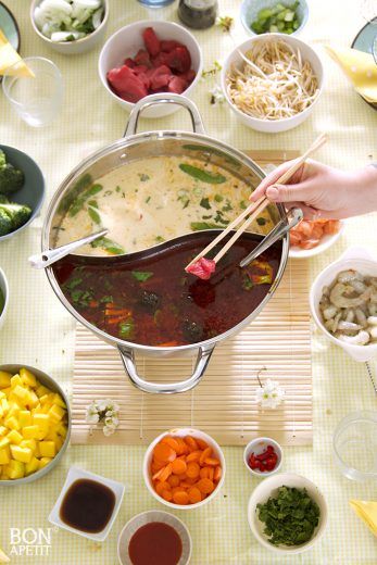 a person holding chopsticks over a pot filled with soup and other foods on a table