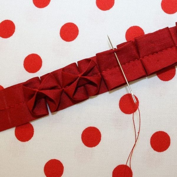 a red piece of fabric with some scissors on it and thread next to it, laying on a polka dot tablecloth