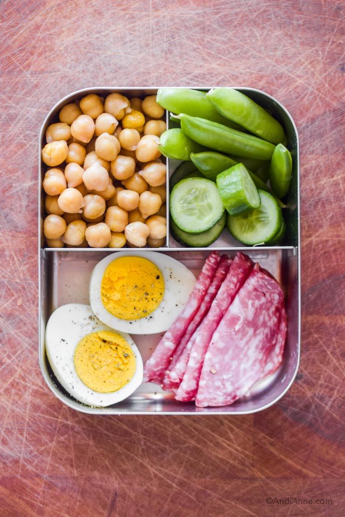 a bento box filled with meat, vegetables and eggs on top of a wooden table