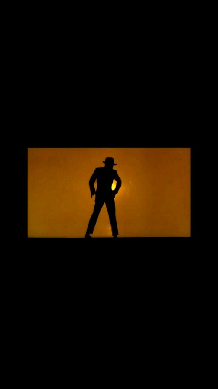 the silhouette of a man wearing a hat and standing in front of an orange background