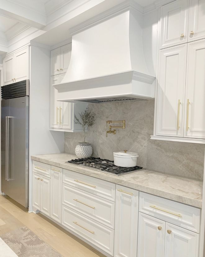 a kitchen with white cabinets and marble counter tops