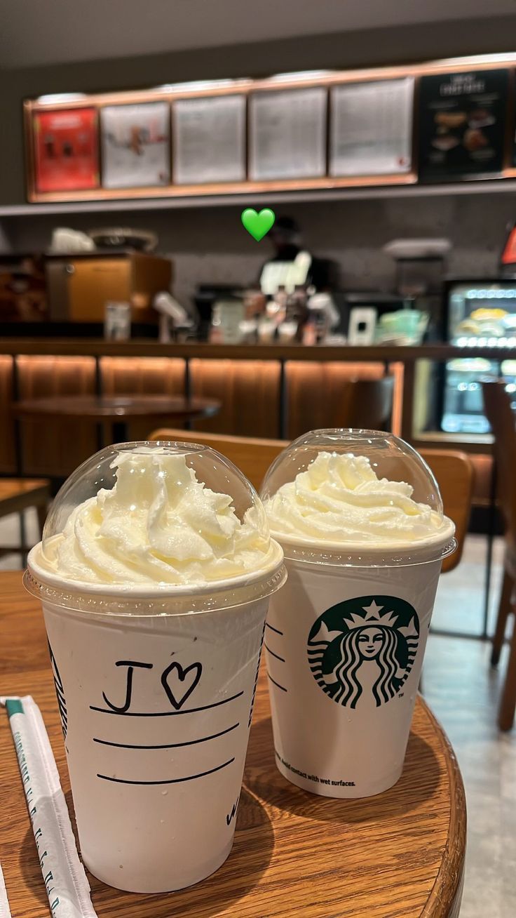 two starbucks drinks sitting on top of a wooden table