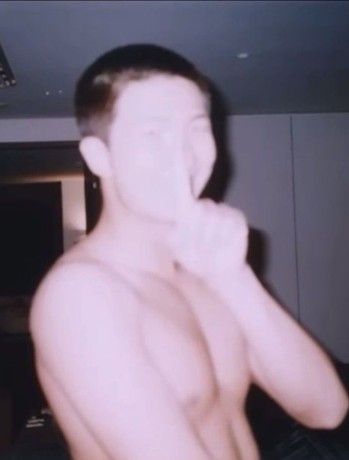 a shirtless man brushing his teeth while standing in front of a mirror with no shirt on