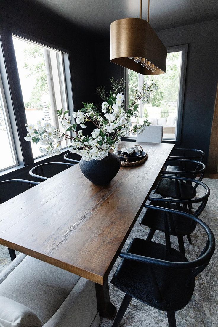 a dining room table with black chairs and flowers in a vase on the centerpiece