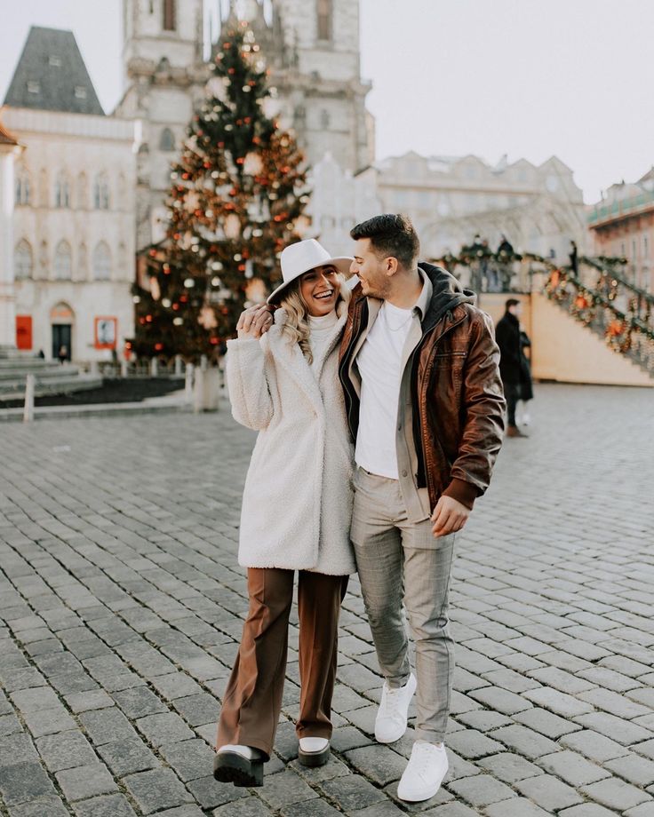 a man and woman standing next to each other in front of a building with a christmas tree